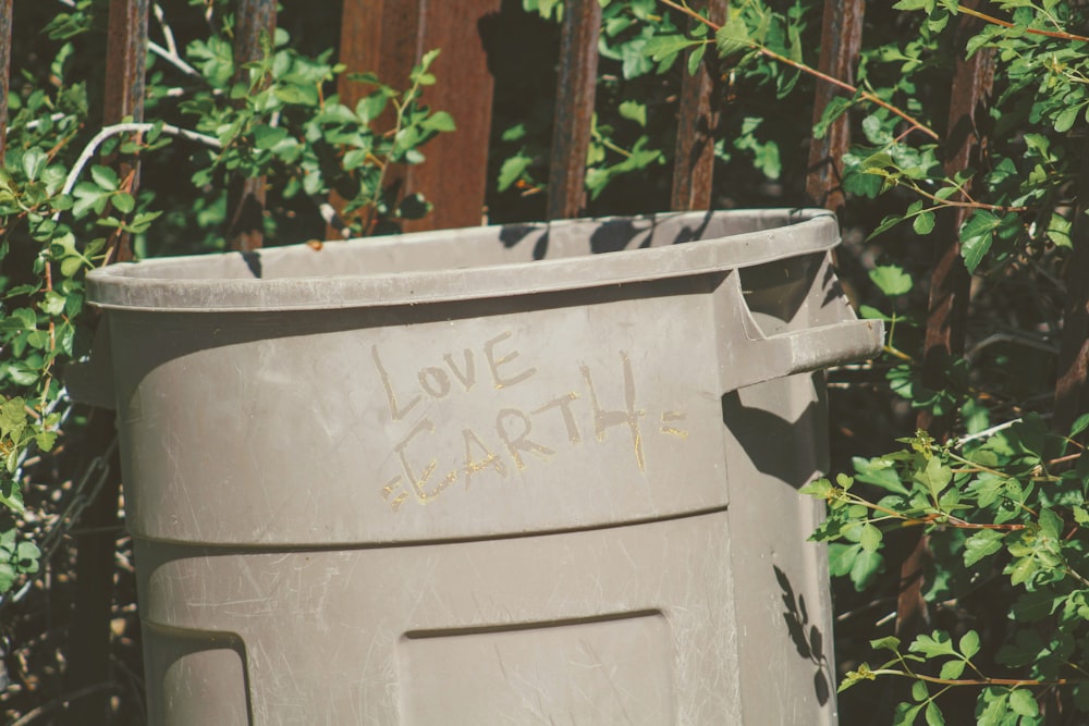 white plastic trash bin beside green plants