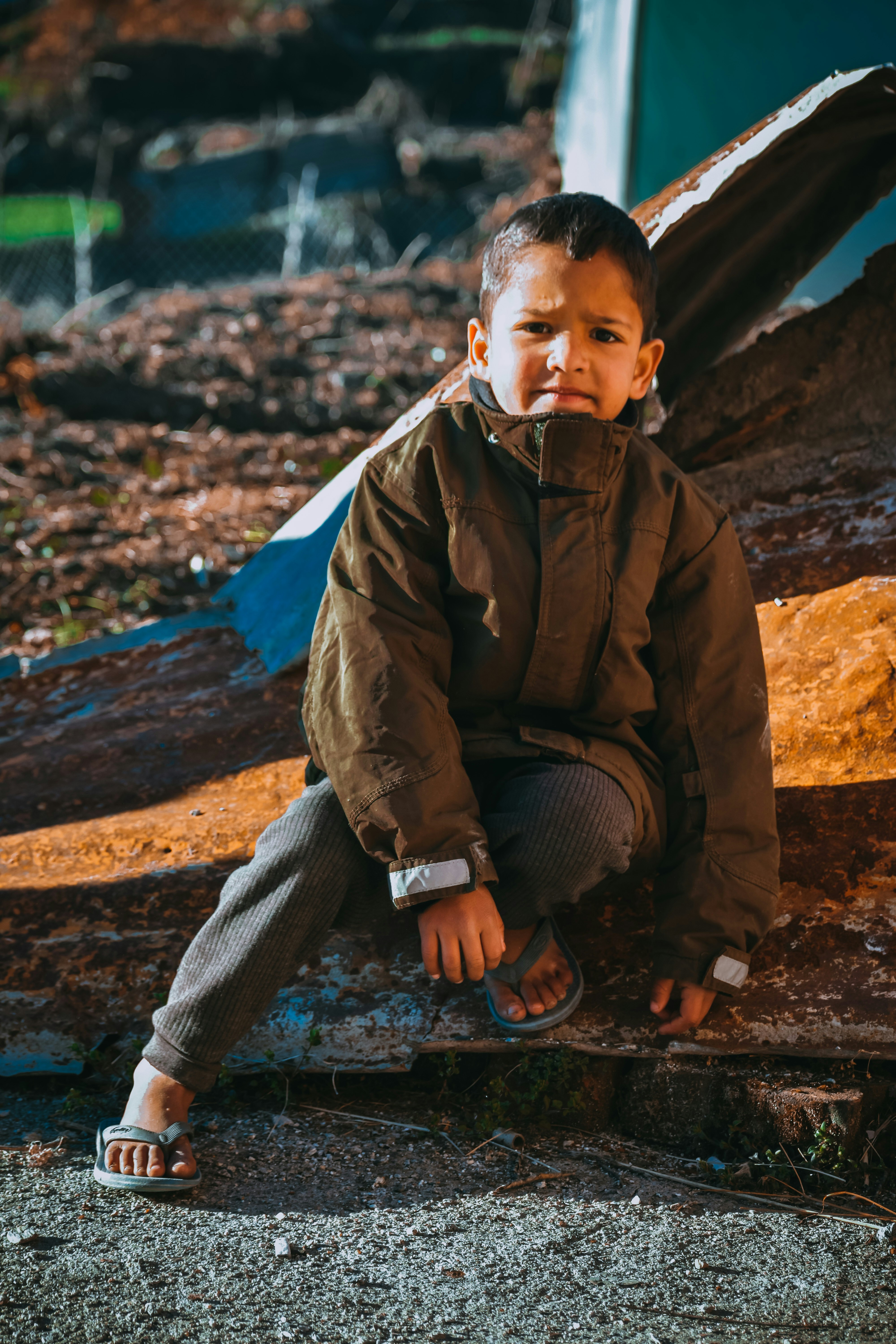 boy in brown jacket sitting on brown rock during daytime
