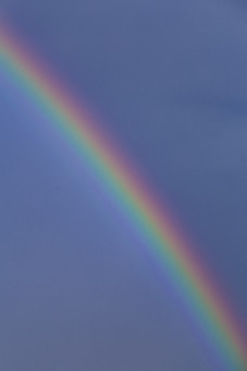 A vibrant rainbow arcs across a cloudy sky, displaying a gradient of colors from red to violet against a backdrop of soft blue and grey tones.