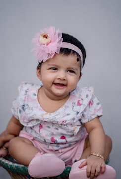 A smiling baby wearing a bright pink bow headband.