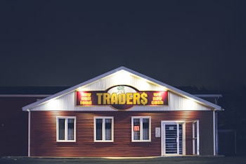 A brightly lit building at night with a sign reading 'TRADER$' and accompanying phrases like 'buy sell lend' and 'we pay cash'. The structure has a red and white facade and is adorned with several windows. A neon 'open' sign is visible in one of the windows.