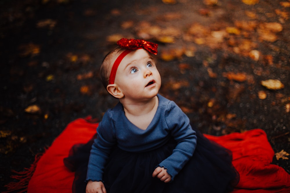 child in blue sweater and red hat sitting on red textile