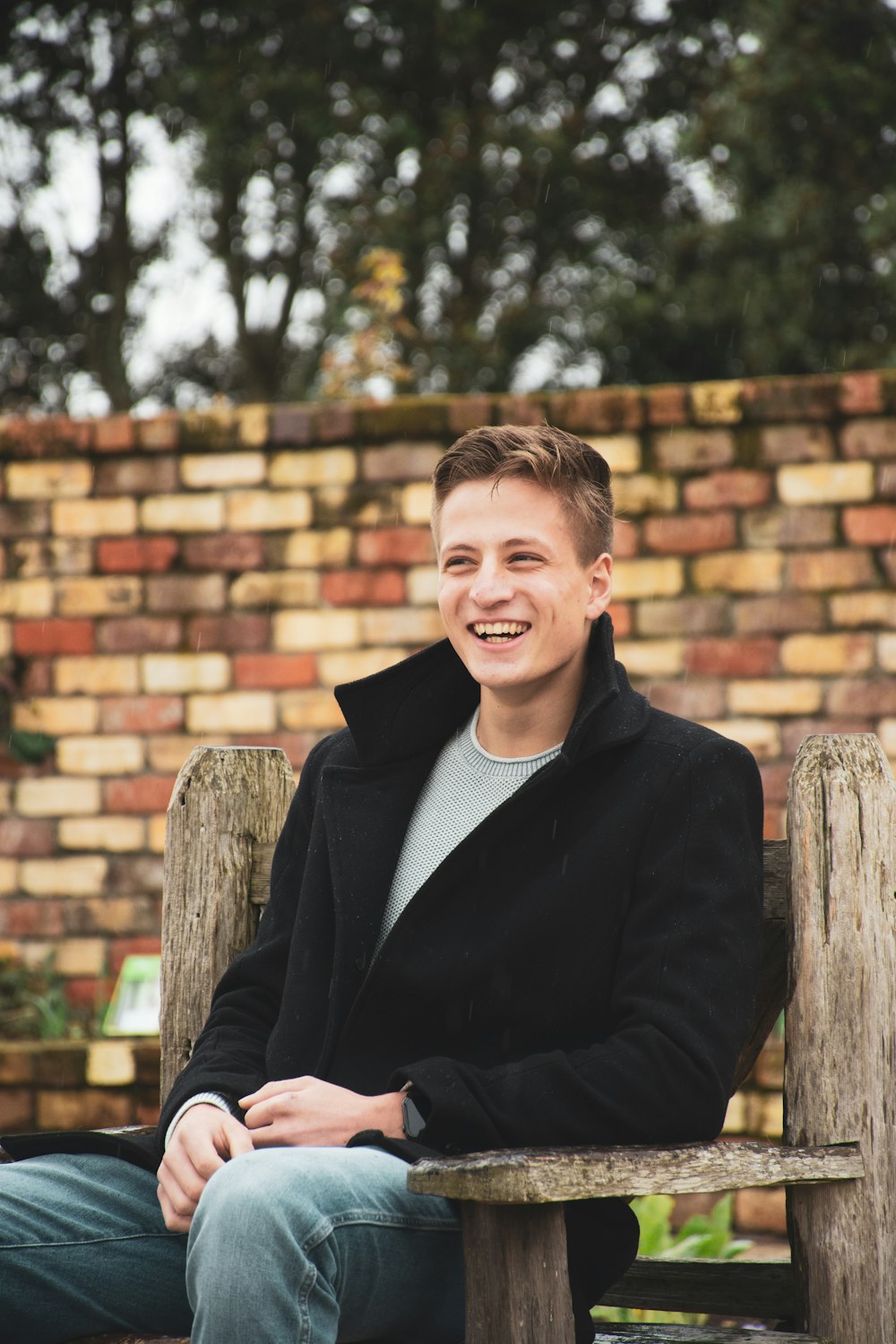 man in black suit jacket sitting on brown wooden bench