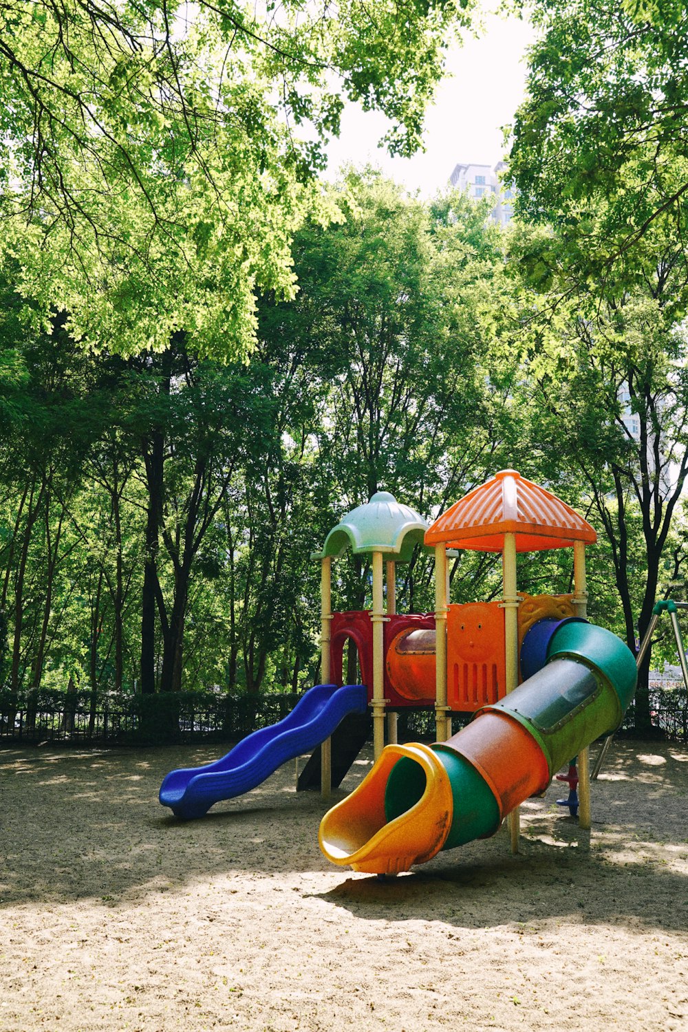 blue and orange slide near green trees during daytime