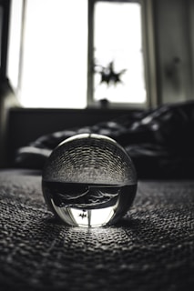 A close-up of a crystal ball resting on a wooden table, reflecting soft light and shadows.