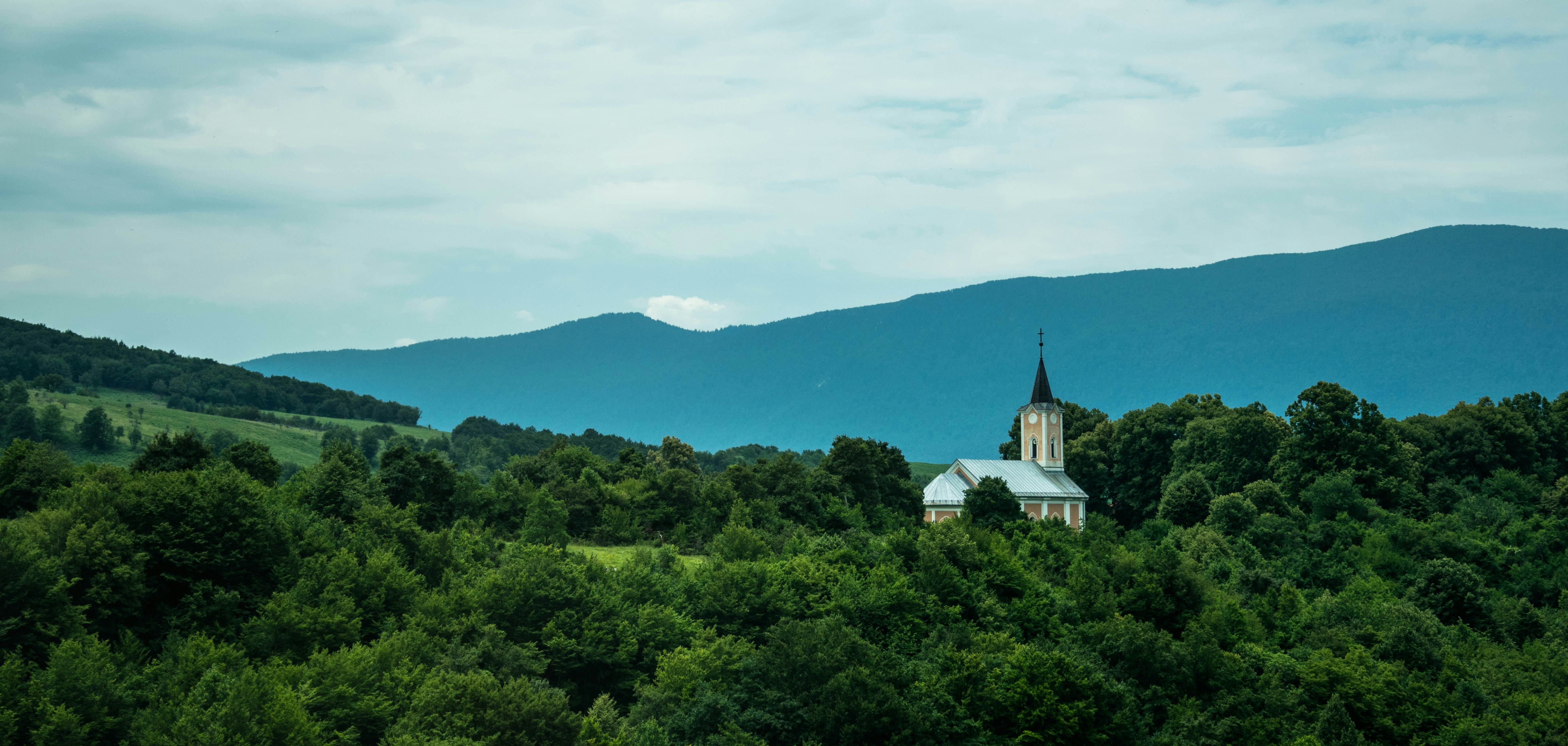 white and gray concrete building surrounded by green trees under white clouds and blue sky during