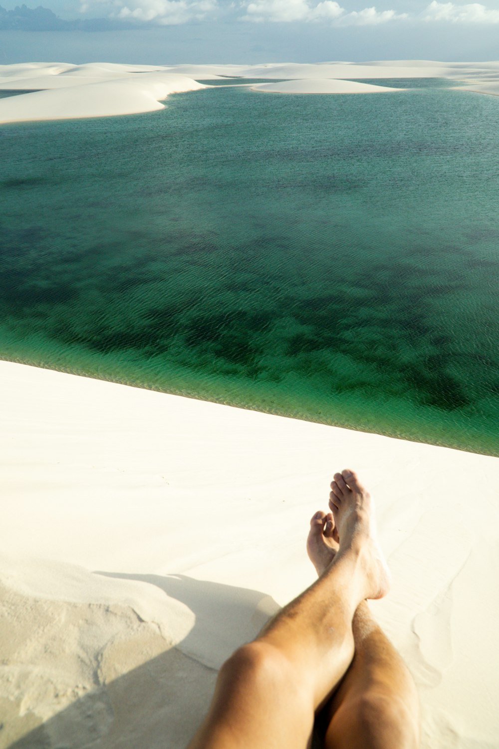 woman lying on white sand near body of water during daytime