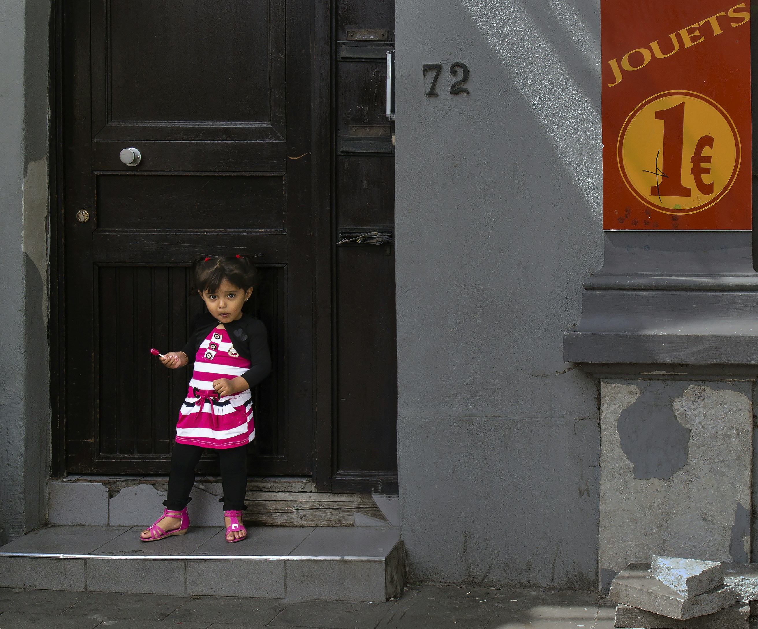 girl in pink and black jacket standing beside black wooden door