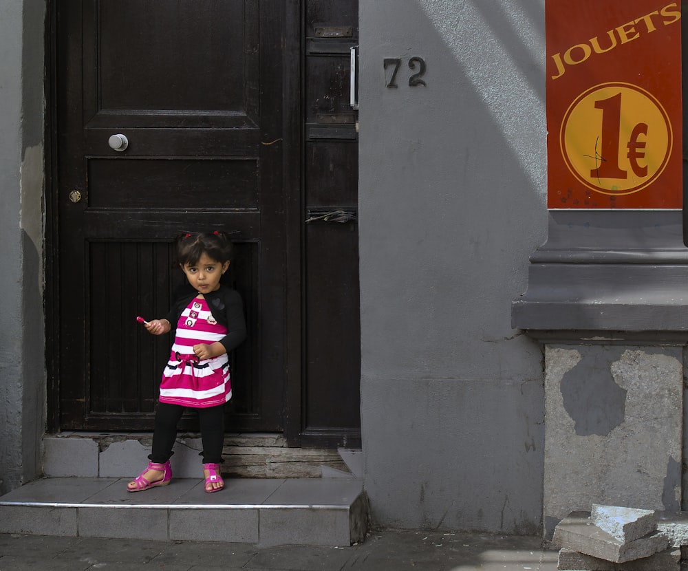 girl in pink and black jacket standing beside black wooden door