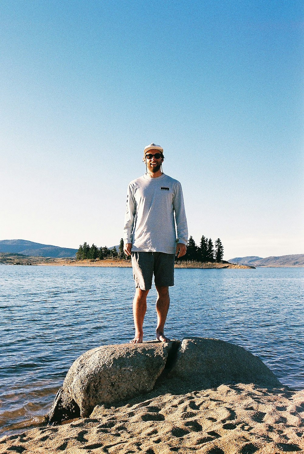 uomo in camicia bianca in piedi sulla roccia vicino allo specchio d'acqua durante il giorno