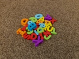 A pile of colorful plastic alphabet letters scattered on a brown carpet.