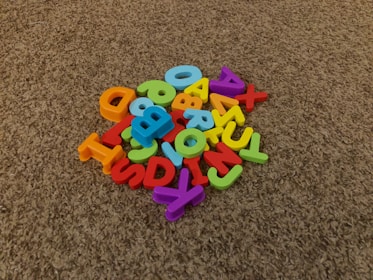 A pile of colorful plastic alphabet letters scattered on a brown carpet.