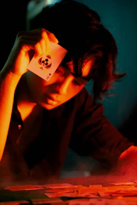 A sinister jester holding a deck of glowing tarot cards under a flickering lantern.