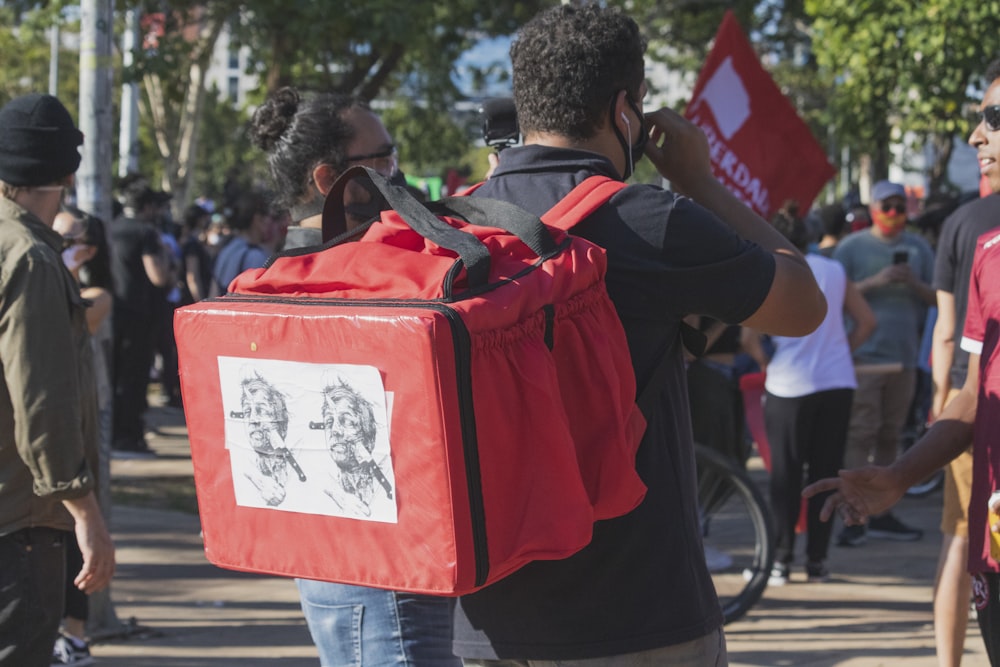 Hombre en mochila roja y negra caminando en la acera durante el día