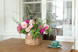 Delicate floral table centerpiece with peach and nude flowers in a rustic vase.