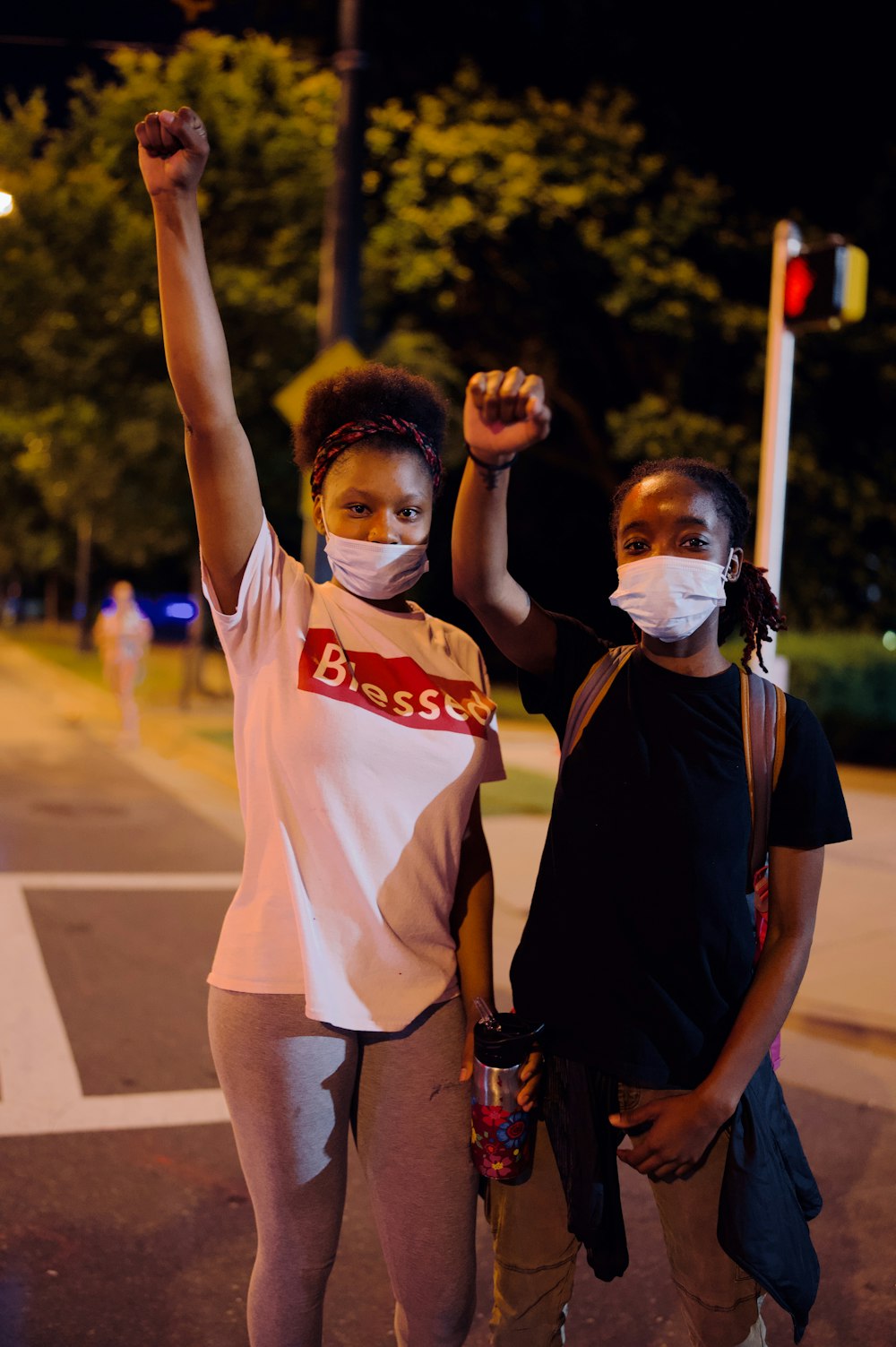 2 women in white and blue shirts standing on road during daytime