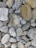 A collection of variously sized and shaped smooth stones, with colors ranging from gray to brown. Some stones have unique textures or patterns, and the arrangement creates a visually interesting mosaic. The scene has a natural, earthy feel.