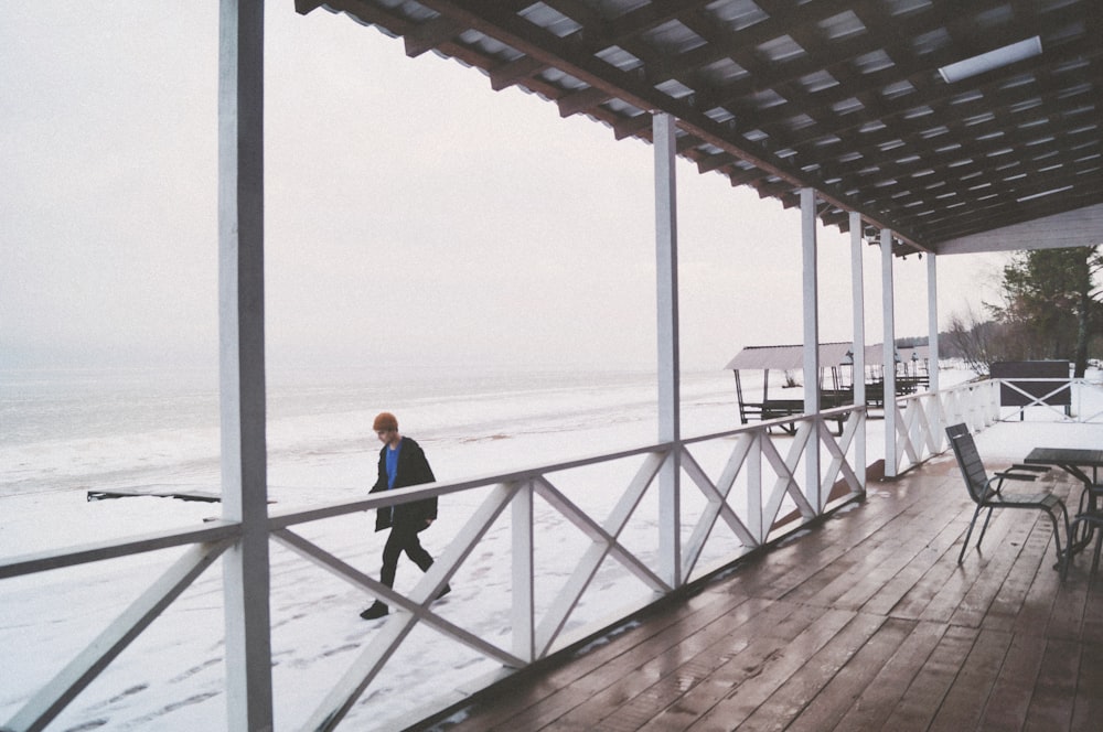 man in black jacket and blue denim jeans walking on wooden dock during daytime