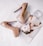 A pair of glossy nude high heel shoes placed on an open fashion magazine page featuring a woman's portrait. A round, transparent glass perfume bottle is positioned nearby.