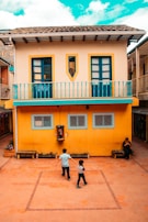 man in white shirt walking beside yellow concrete building during daytime