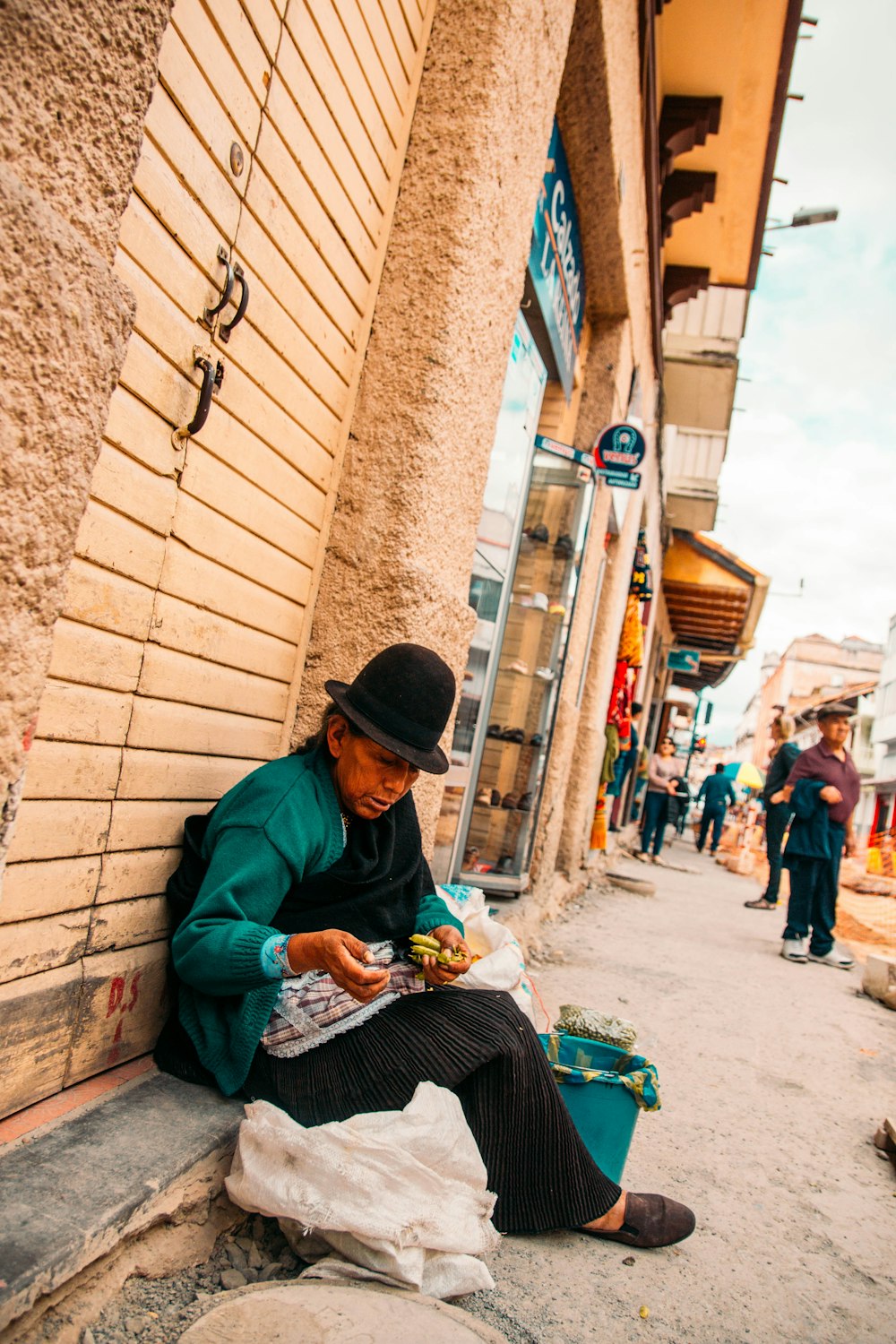 homme en chemise à manches longues verte assis sur le trottoir pendant la journée