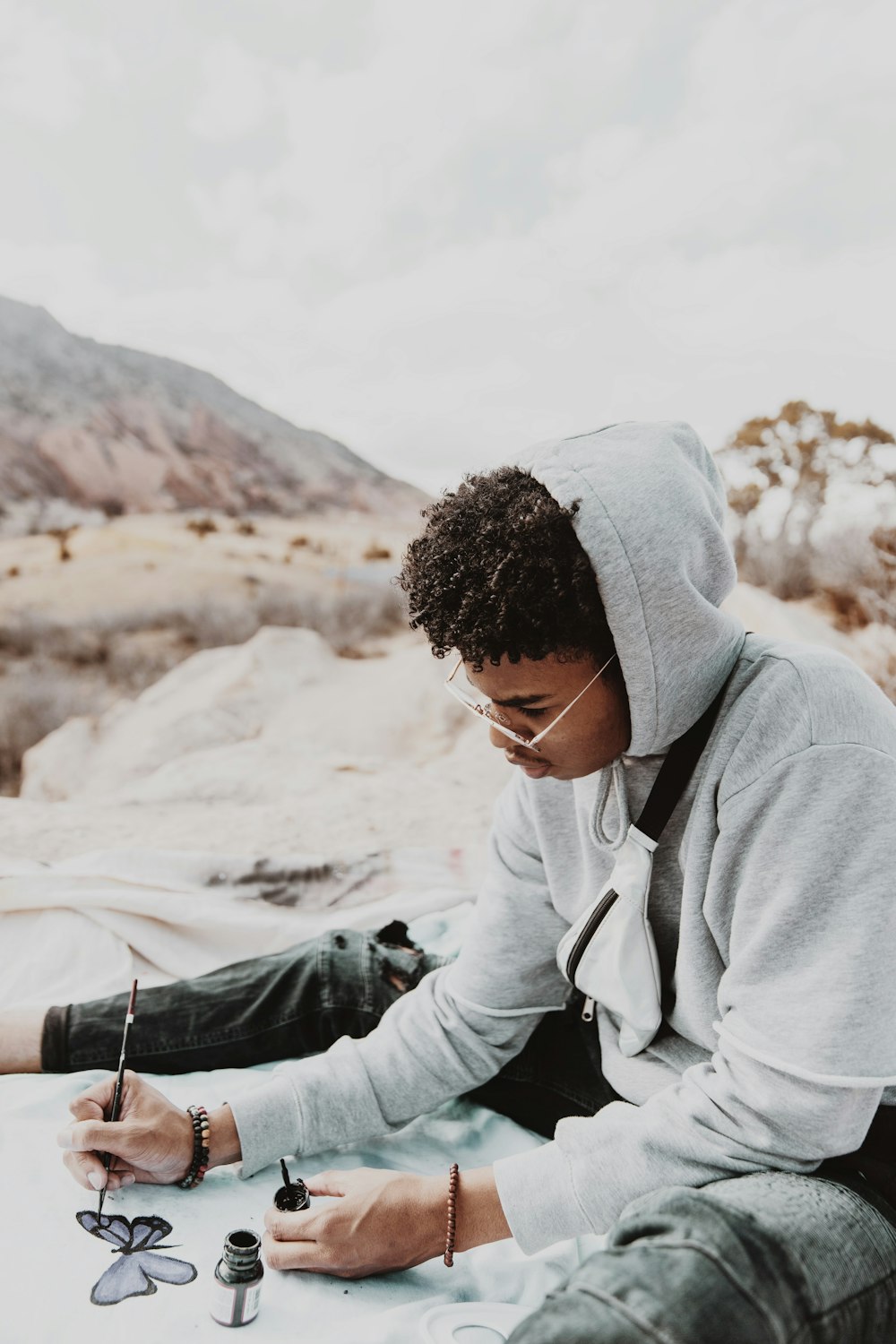 man in gray hoodie and black knit cap sitting on white sand during daytime