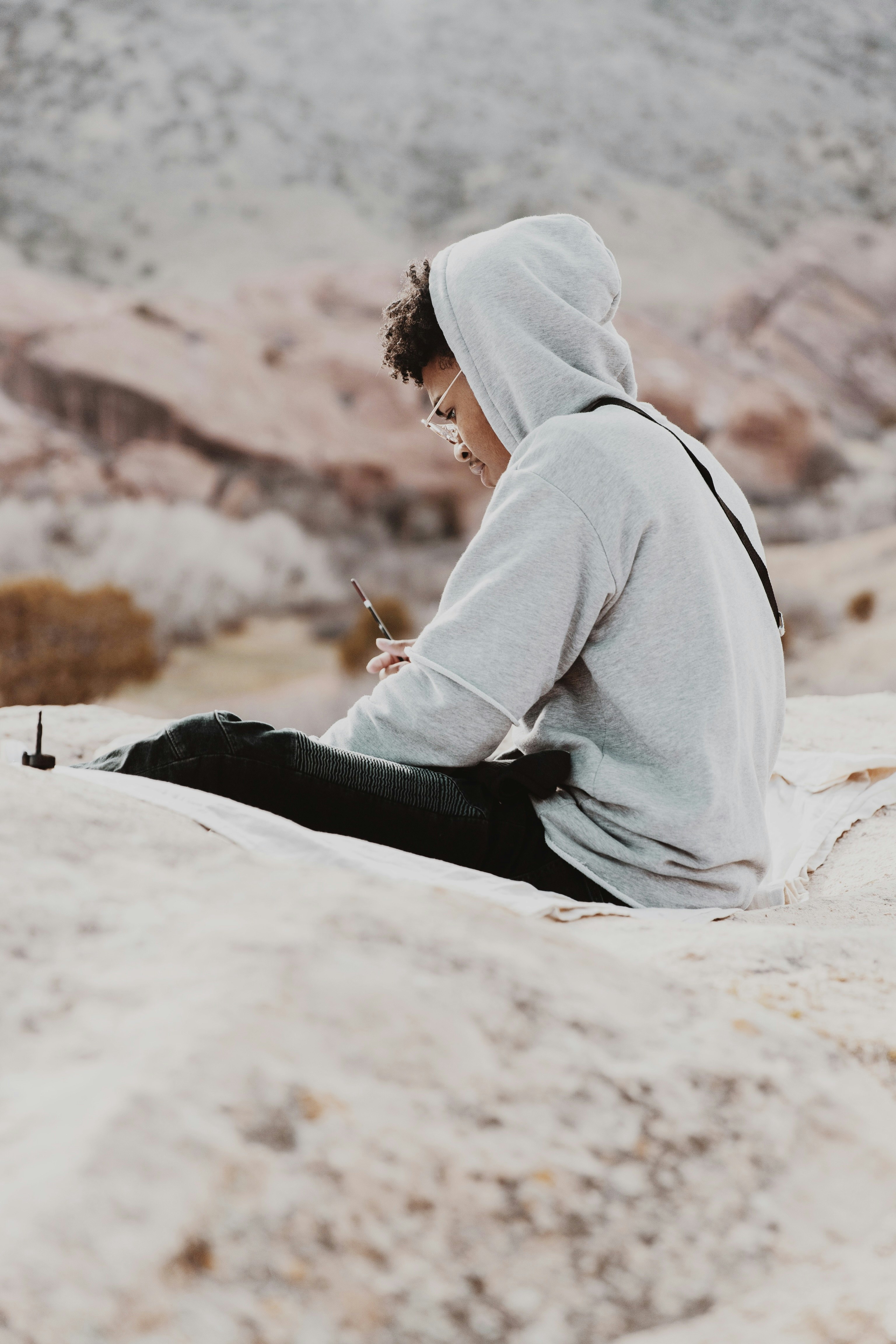 woman in gray hoodie and black pants sitting on white sand during daytime