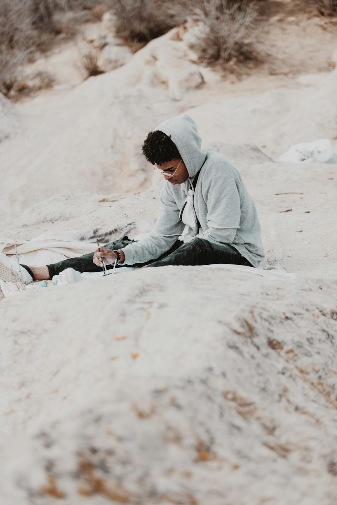 man in gray hoodie sitting on white sand during daytime