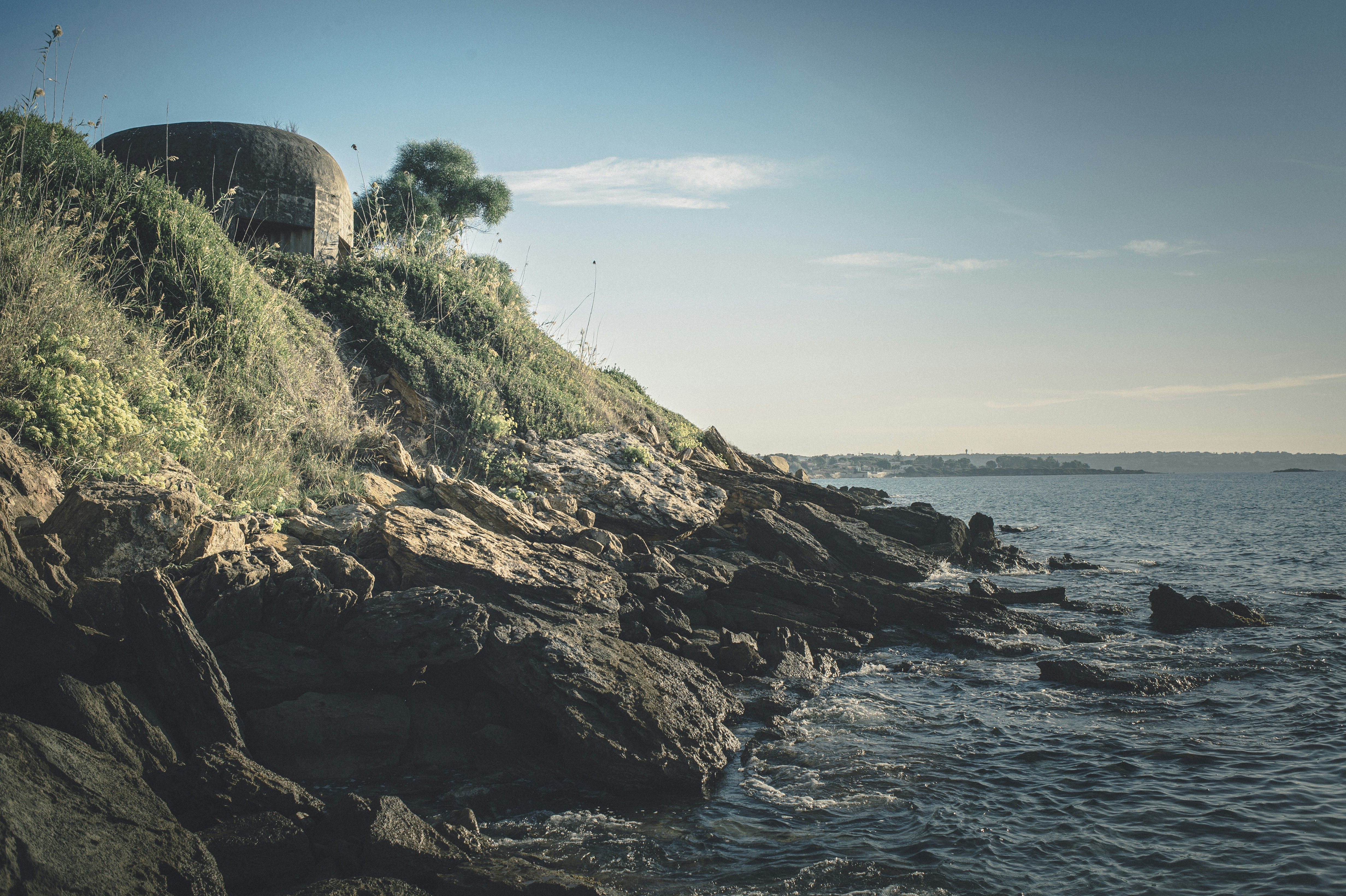 brown rock formation near body of water during daytime, World War II pillbox on the coast of Sicily.