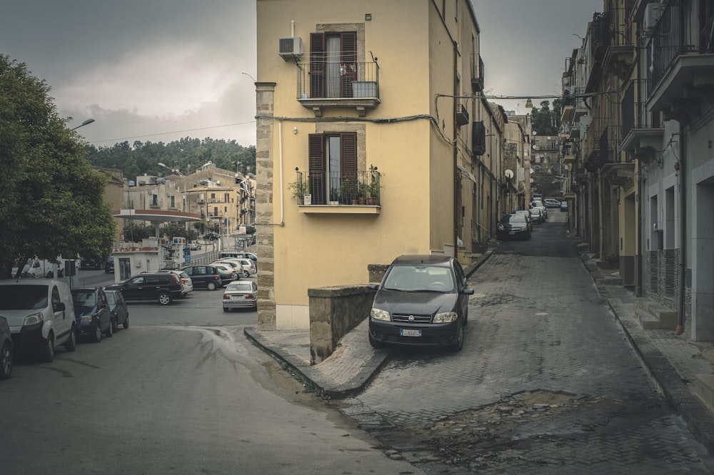 Coche negro aparcado junto a un edificio de hormigón amarillo durante el día