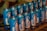 Multiple blue cans featuring images and text in an organized display, possibly representing a religious or spiritual theme. The design on the cans includes a depiction of a figure resembling religious icons, and the text is in a foreign language, suggesting a cultural context.