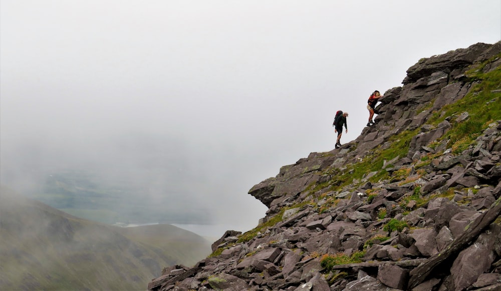 2 person standing on rocky mountain during foggy weather