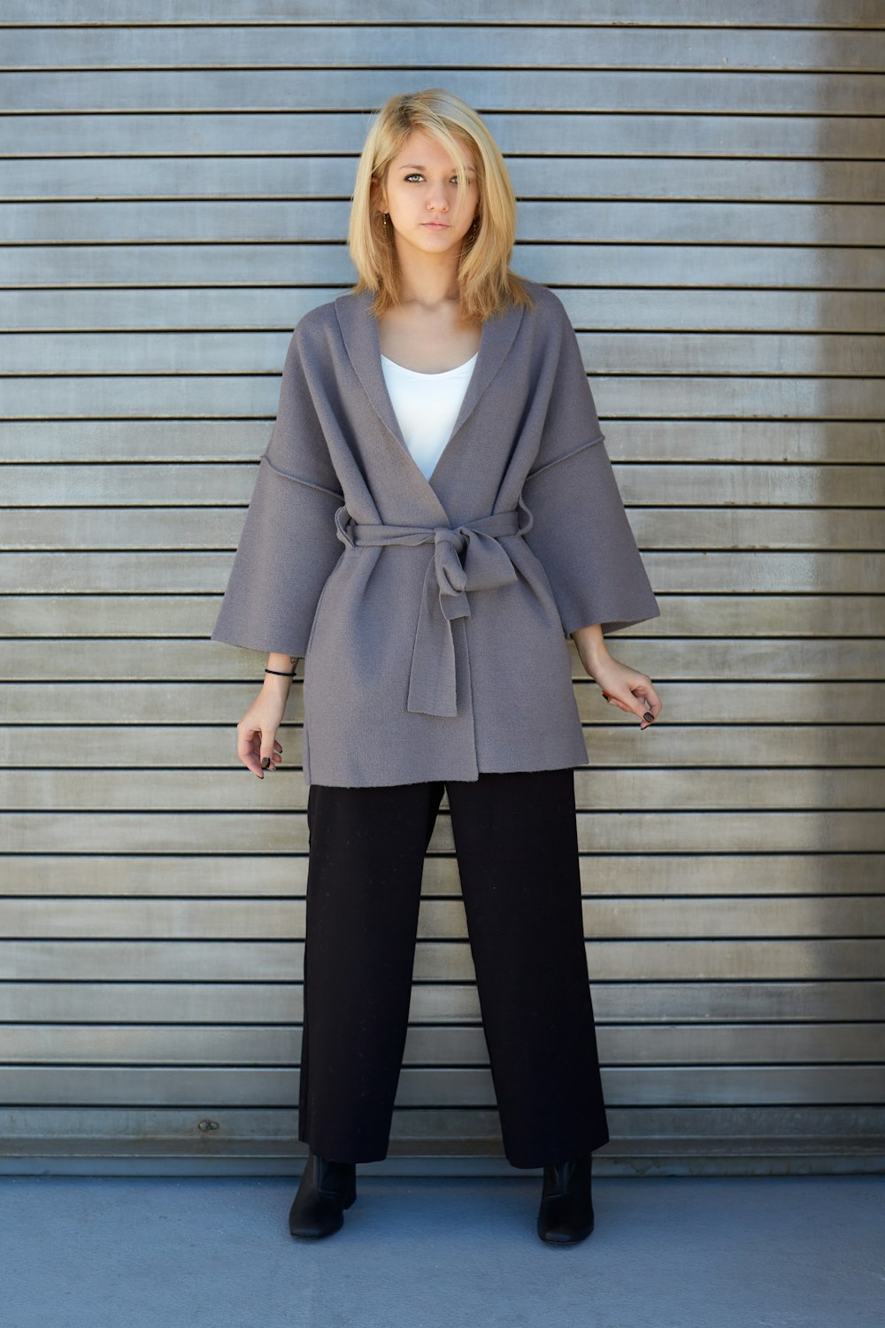 woman in gray blazer and black pants standing beside gray wall
