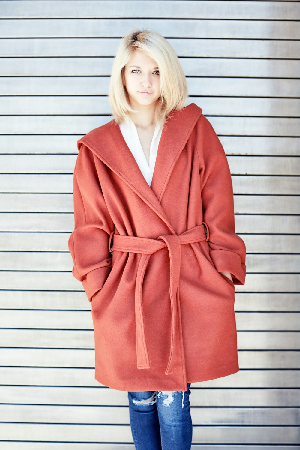 woman in red coat standing beside white wall