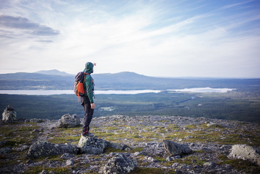 man in blue jacket standing on rock formation looking at the sea during daytime