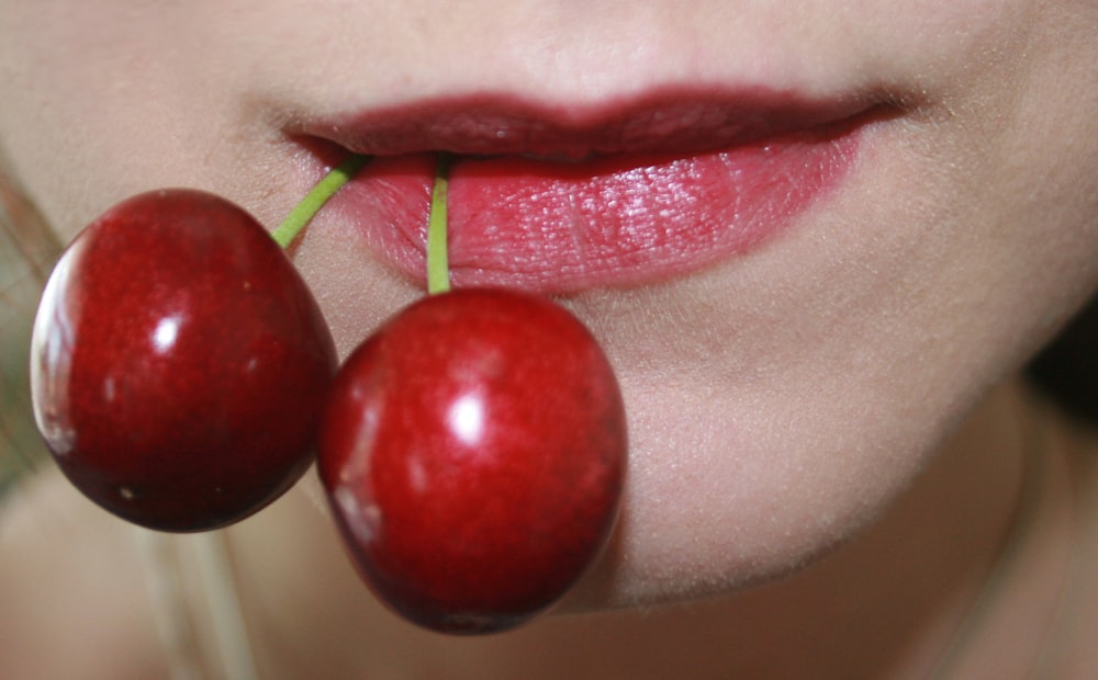 person with red round fruit on mouth