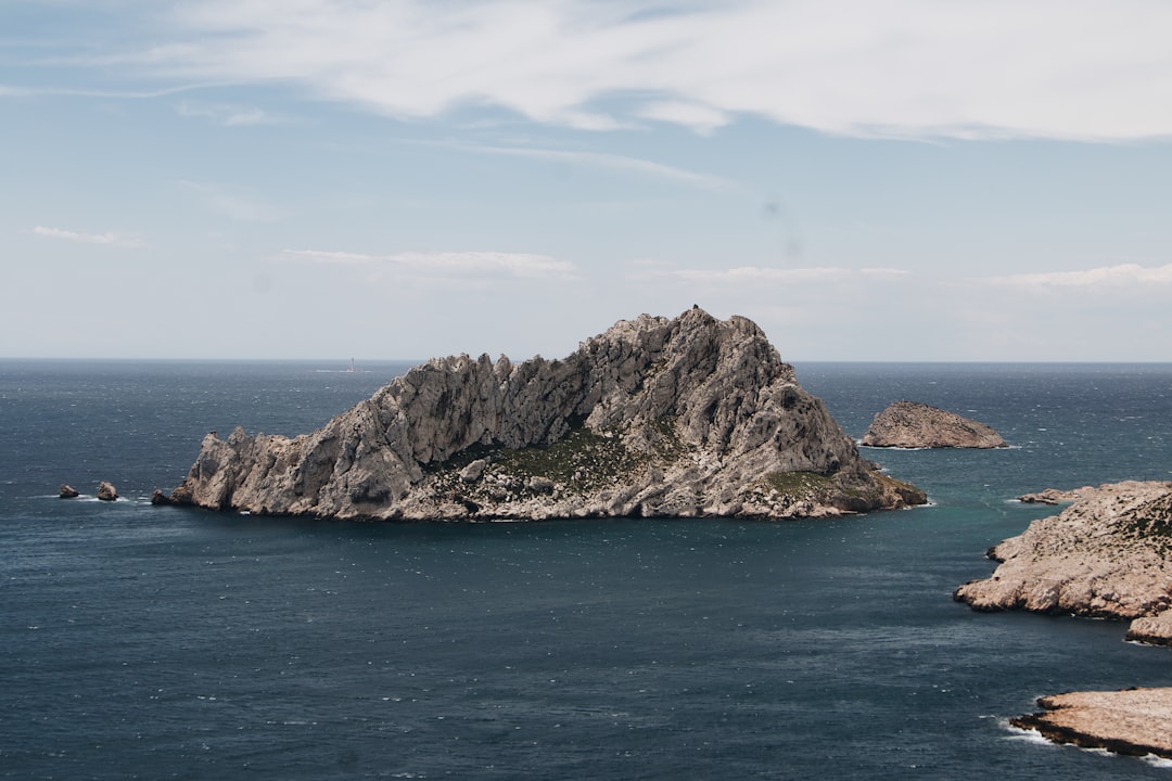 gray and green rock formation on blue sea under blue and white cloudy sky during daytime