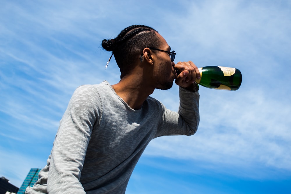 man in gray crew neck long sleeve shirt drinking green bottle under blue and white sunny