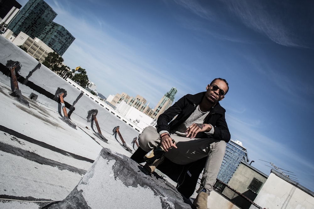 man in black jacket sitting on gray concrete wall during daytime