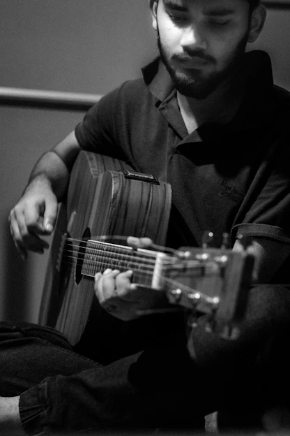 Black and white photo of a musician deeply focused while playing an acoustic guitar in a minimalist studio setting.