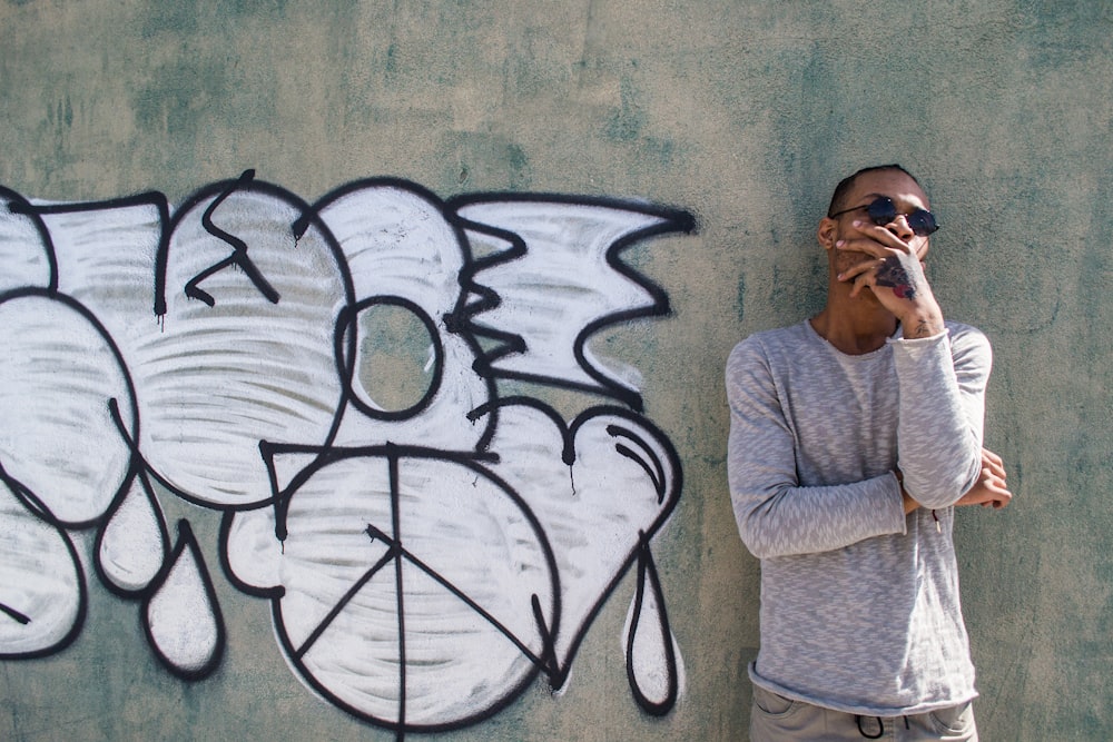 man in gray sweater standing beside wall with graffiti