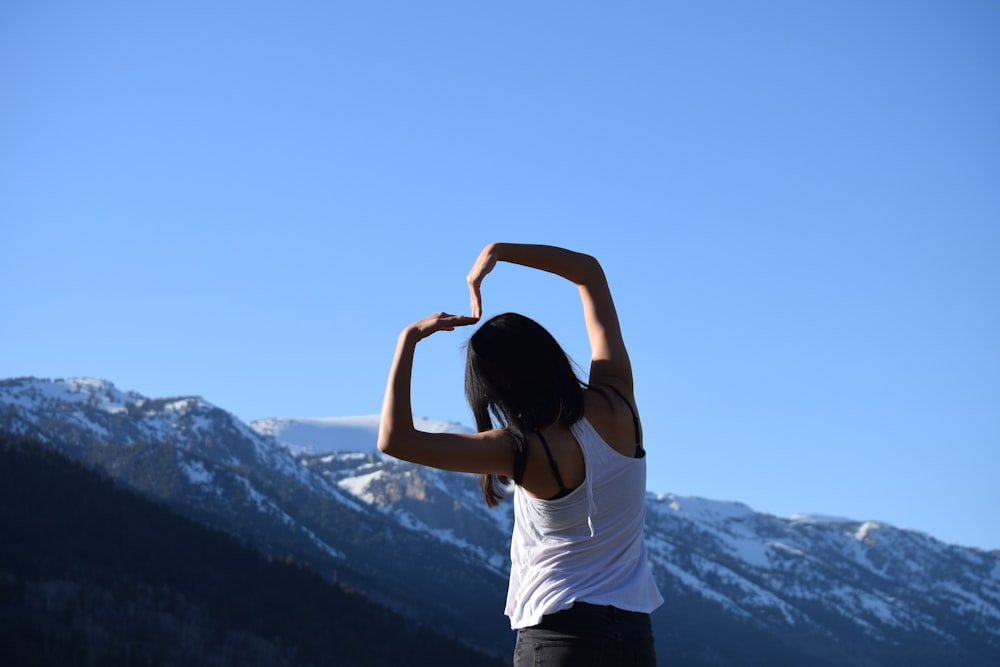 woman in white t-shirt and black pants standing on top of mountain during daytime