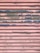 A metal surface with horizontal slats showing a distressed texture. The surface is painted in pink with worn-out blue sections, giving it a rustic look.