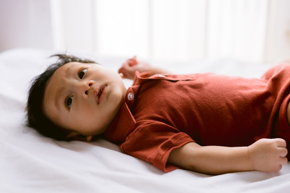 빨간 셔츠를 입은 아기가 침대에 누워 있다