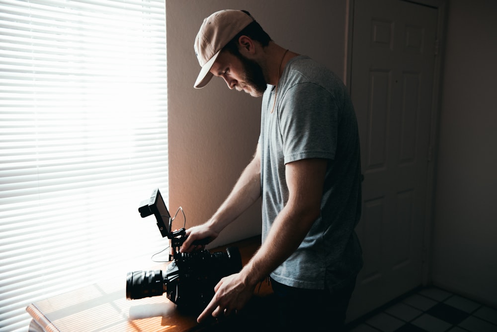 man in gray crew neck t-shirt and gray cap holding black video camera