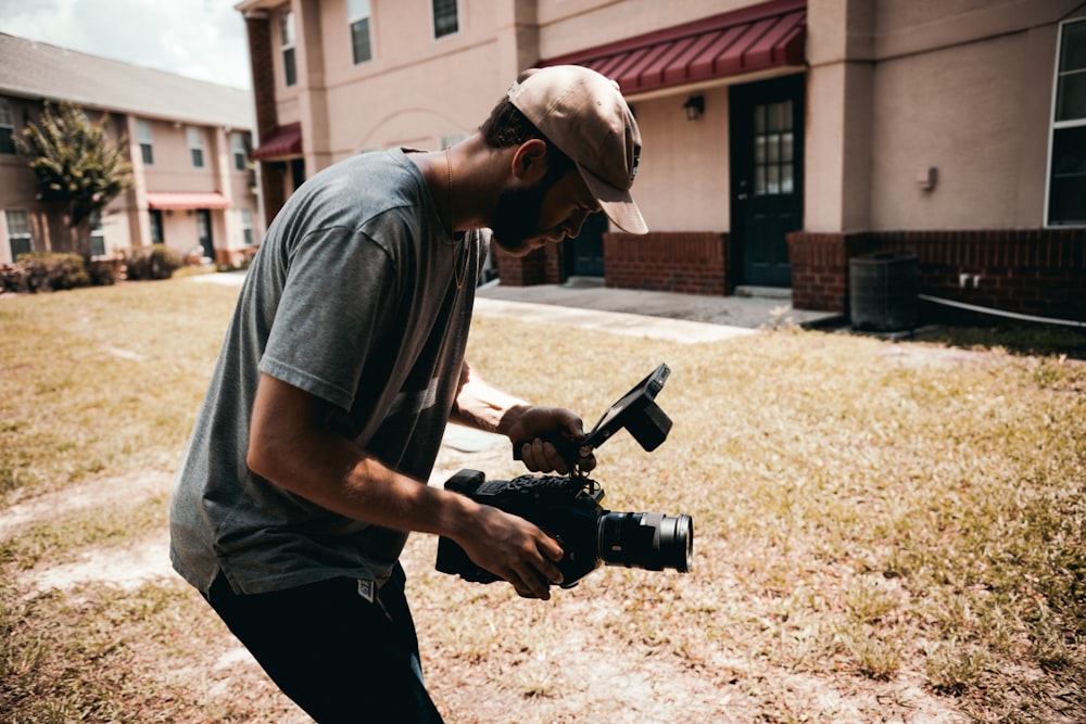 man in gray t-shirt and black pants holding black dslr camera