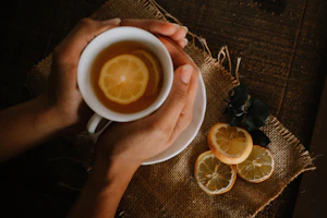 A hand holding a dropper with green propolis extract dripping into a cup of warm tea