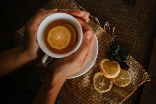 A hand holding a dropper with green propolis extract dripping into a cup of warm tea