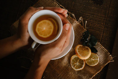 A warm cup of de'mure lemon honey tea on a rustic wooden table with fresh lemon slices and honey jar nearby.