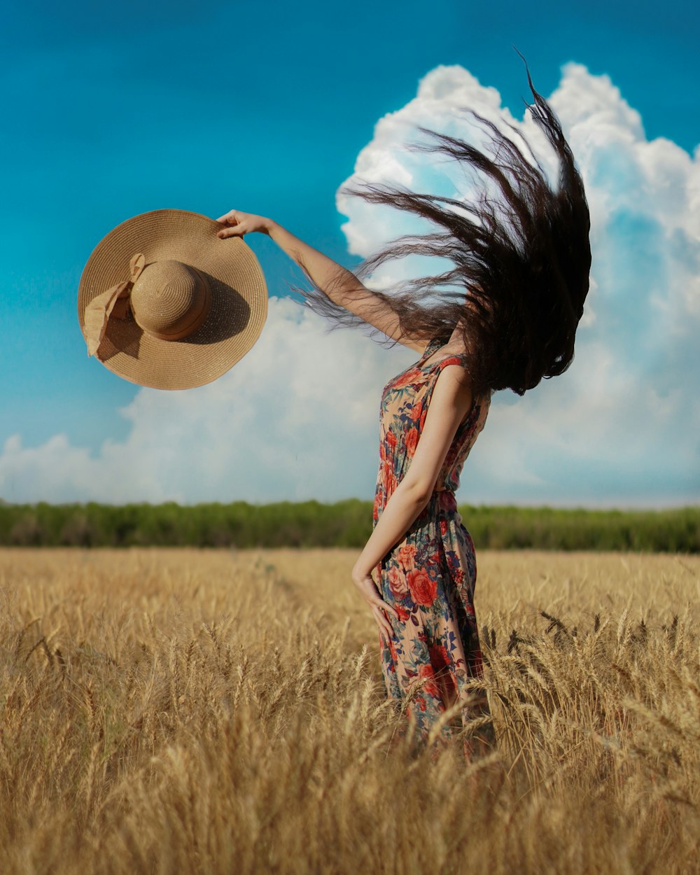woman in red and white floral dress with brown straw hat standing on brown grass field